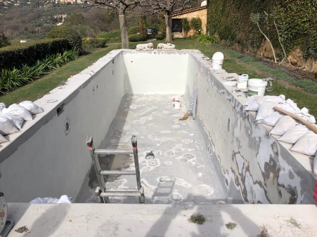 Rénovation de piscine en extérieur : murs et fond en cours de préparation avec un enduit clair. Équipement de chantier, dont un seau CALIXTONE.