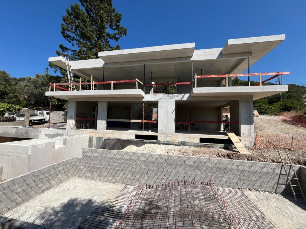 Construction d'une maison moderne en béton brut, vue sur la structure et le coffrage d'une piscine.