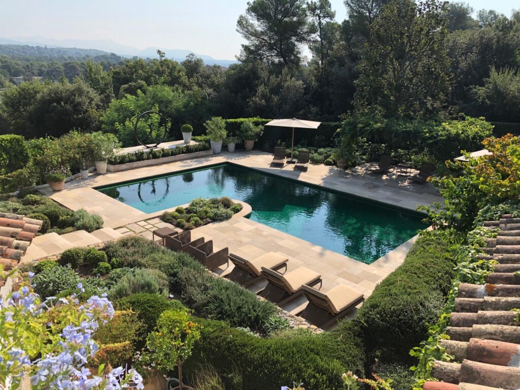 Piscine rectangulaire aux eaux turquoise entourée de dalles de pierre, bains de soleil et végétation luxuriante méditerranéenne en Provence.