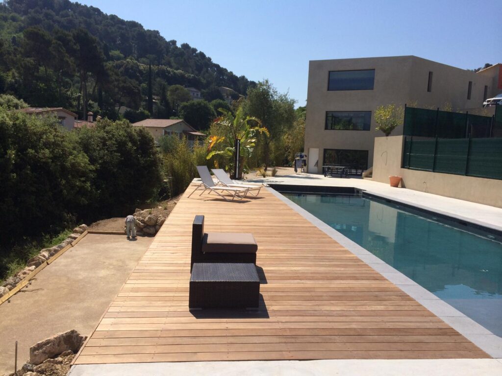 Terrasse en bois près d'une piscine moderne, vue sur une colline boisée et une maison contemporaine.